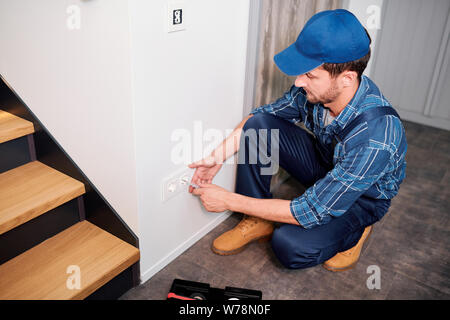 Elettricista professionale in indumenti da lavoro per il controllo o la misurazione della tensione della presa Foto Stock