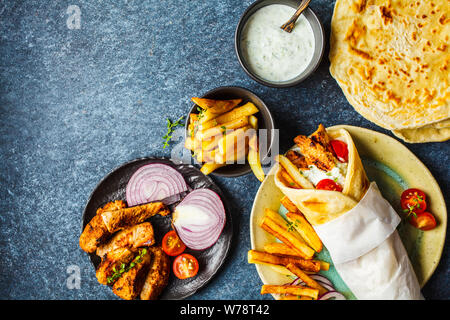 Gyros souvlaki avvolge in pane pita con pollo, patate e salsa tzatziki, sfondo blu, vista dall'alto. Foto Stock