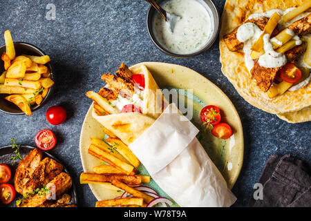 Gyros souvlaki avvolge in pane pita con pollo, patate e salsa tzatziki, sfondo blu, vista dall'alto. Foto Stock