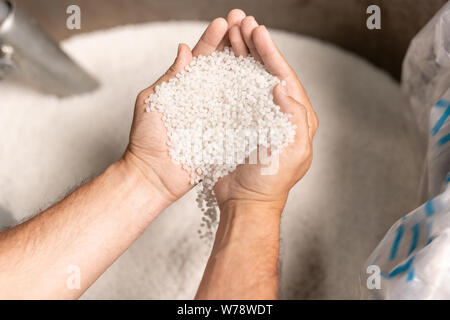 Vista del moderno stabilimento lavoratore mani pila di bianco di pellet di polimero Foto Stock