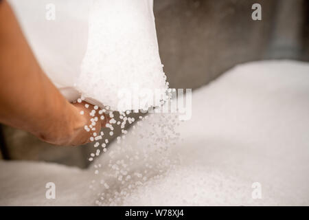 Piccoli granuli di plastica scattering fuori del sacco bianco detenuto dal lavoratore Foto Stock
