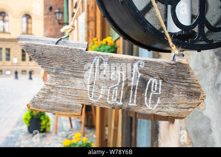 Caffè scritto su una freccia a forma di base di legno vecchio stile, retrò, con edifici vecchi e fiori su sfondo Foto Stock