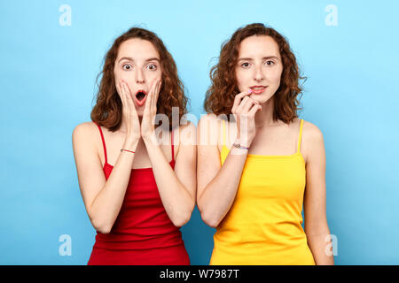 Ritratto di belle gemelle in rosso e giallo tshirt mostrare le emozioni e sensazioni . sorpreso le ragazze non possono credere in qualcosa. close up phot Foto Stock