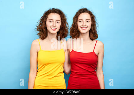 Gioiosa identico positivo gemelli elegante in rosso e giallo di sposa guardando la telecamera. close up photo isolati a sfondo blu, lifestyle, doppia b Foto Stock