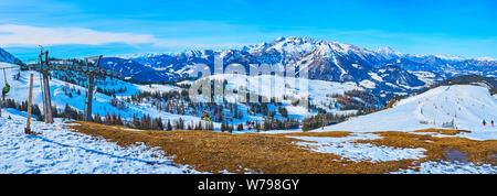 Uno scenario mozzafiato di Dachstein West Alpi coperte di neve e foreste di pini, con una vista sul veloce seggiovia di equitazione con gli sportivi, andando a a Foto Stock