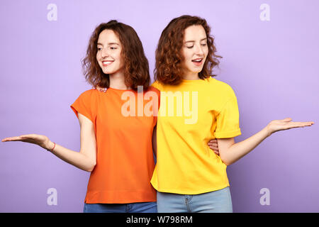 Bella identiche alle sorelle gemelli azienda copyspace sulle palme isolate su uno sfondo blu, ragazze offrono scelta, scala, donna pensando di advant Foto Stock