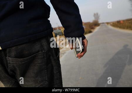 Il 15-anno-vecchio ragazzo cinese cammina su una strada con il suo smartphone in un villaggio della città di Jilin, a nord-est della Cina di provincia di Jilin, 4 novembre 2017. 15- Foto Stock