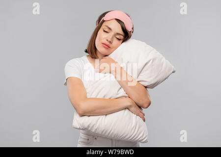 Giovane femmina tranquilla abbracciando cuscino mantenendo la sua testa su di esso Foto Stock