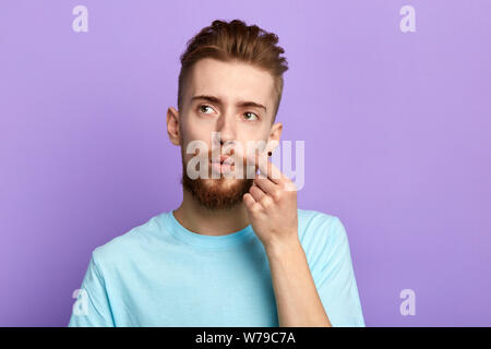Malinconici, elegante uomo bello toccando i suoi baffi cercando isolati a sfondo blu. studio shot. Tempo libero Tempo libero Foto Stock