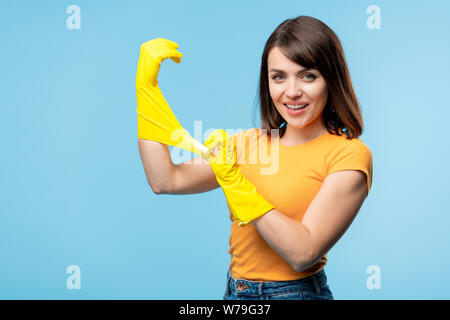 Felice giovane massaia in giallo t-shirt mettere dei guanti di gomma sulle mani Foto Stock
