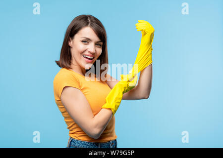 Giovane governante mettendo su giallo guanti di gomma prima di faccende di casa Foto Stock
