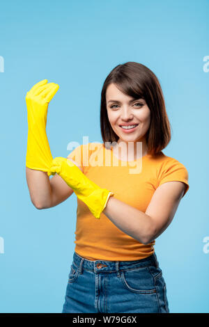 La governante o servizio di pulizia personale mettendo giallo guanti in gomma sulle mani Foto Stock