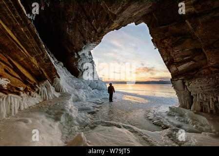 Viaggiando in inverno, un uomo in piedi sul lago ghiacciato Baikal con grotta di ghiaccio in Siberia, Russia Foto Stock