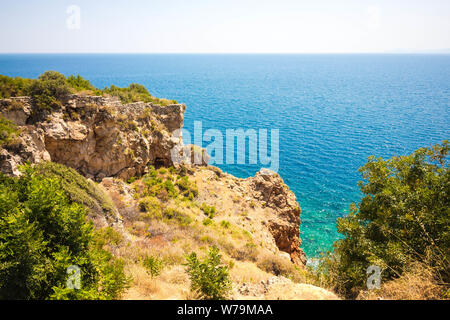 Bella vista dalla scogliera sul mare. L'acqua è trasparente con una tonalità di blu. Boccole e varie vegetazione crescere sulla roccia. Foto Stock