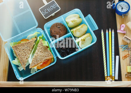 Scuola blue scatola di pranzo con sandwich fatti in casa, mela verde, cookie, matite, orologio, notebook sul tavolo. Mangiare sano a scuola. Si torna a scuola Foto Stock