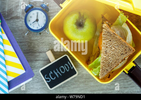 Scuola giallo scatola di pranzo con sandwich, mela verde, orologio sulla lavagna. Mangiare sano a scuola. Si torna a scuola dello sfondo. Appartamento laico, vista dall'alto. Foto Stock