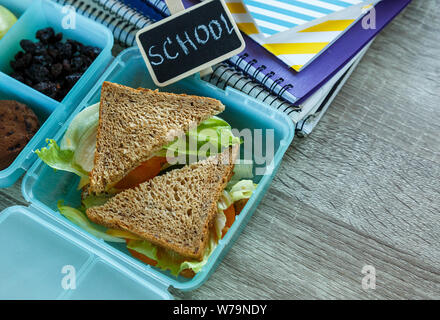 Scuola blue scatola di pranzo con sandwich fatti in casa, mela verde, cookie, matite, orologio, notebook sul tavolo. Mangiare sano a scuola. Si torna a scuola Foto Stock