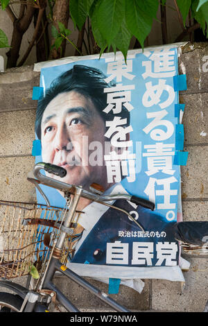 Shinzo Abe poster, leggermente sbiadite, attaccato ad un muro di cemento dietro una bicicletta parcheggiata; Tokyo, Giappone Foto Stock