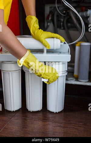 Plumber in giallo guanti per la casa cambia filtri per l'acqua. Repairman installazione di acqua le cartucce del filtro in cucina. Acqua potabile sistema di filtrazione i Foto Stock