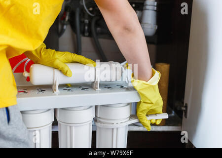 Plumber in giallo guanti per la casa cambia filtri per l'acqua. Repairman installazione di acqua le cartucce del filtro in cucina. Acqua potabile sistema di filtrazione Foto Stock