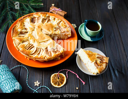 Torta di frutta per il Natale decorato con mele sulla piastra di colore arancione con la tazza di caffè sul tavolo di legno. Delicioius dolci fatti in casa. Anno nuovo Foto Stock
