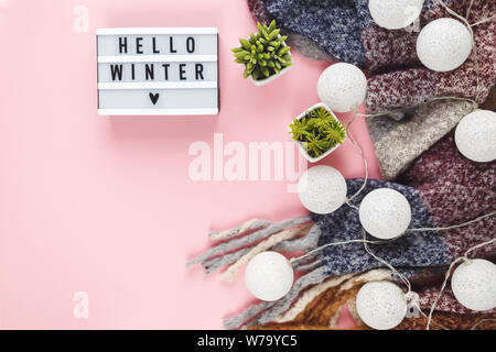 Concetto di Natale lay piatto. Caldo e accogliente bianco inverno maglione abbigliamento, Lightbox e decorazioni di Natale cornice rosa su sfondo pastello Foto Stock