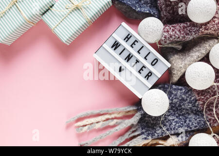 Concetto di Natale lay piatto. Caldo e accogliente bianco inverno maglione abbigliamento, Lightbox e decorazioni di Natale cornice rosa su sfondo pastello Foto Stock