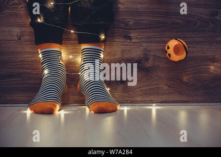 Kids gambe in caldo stile luminoso a strisce colorate divertenti calzini in ghirlanda di luci sul pavimento con le zucche in camera. Arredo per Halloween, accogliente in questo momento. Foto Stock