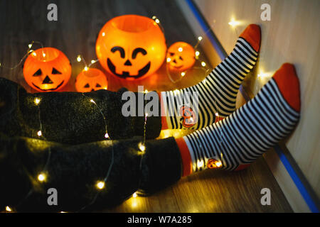 Kids gambe in caldo stile luminoso a strisce colorate divertenti calzini in ghirlanda di luci sul pavimento con le zucche in camera. Arredo per Halloween, momento accogliente Foto Stock