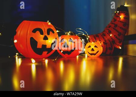 Kids gambe in caldo stile luminoso a strisce colorate divertenti calzini in ghirlanda di luci sul pavimento con le zucche in camera. Arredo per Halloween, accogliente in questo momento. Foto Stock