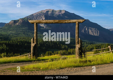 Un rustico cancello di legno del vecchio weathered log in un tipico western USA scena di campi, foreste e un elevato picco di montagna su un ranch nelle Montagne Rocciose Foto Stock