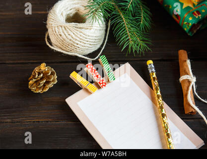 Preparazione per il natale - Blocco note per creare un elenco di regali per amici e familiari sullo sfondo di legno Foto Stock