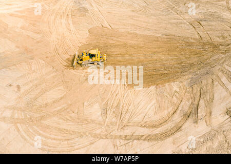 Giallo industriale bulldozer livellamento del terreno prima della costruzione della strada, vista dall'alto Foto Stock