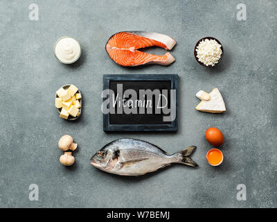 Vaitamin fonti d concetto. Pesci, salmone, latticini, uova, funghi e lavagna con vitamina D di parole sulla pietra grigia sullo sfondo. Vista superiore piatta o laici. Foto Stock