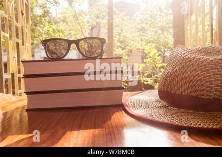 Vista laterale anteriore del libro e occhiali da sole con un cappello di paglia. Estate vacanze la nozione di sfondo. Foto Stock