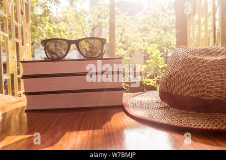 Vista laterale anteriore del libro e occhiali da sole con un cappello di paglia. Estate vacanze la nozione di sfondo. Foto Stock