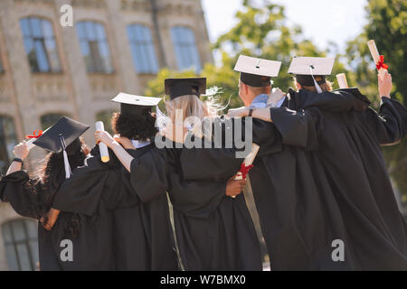 I laureati che abbraccia ogni altra in piedi in cantiere. Foto Stock