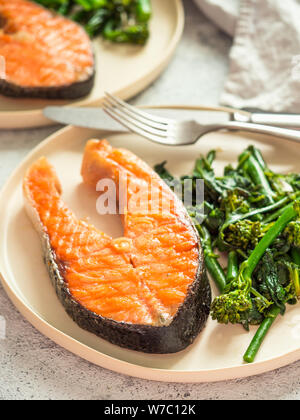 Pronto a mangiare salmone alla griglia bistecca e verdi - baby broccoli o broccolini e spinaci su rustiche piastra artigianali su sfondo grigio. Dieta cheto piatto. In verticale Foto Stock