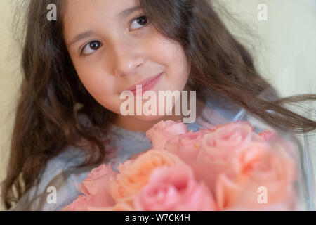 Ritratto di una ragazza adolescente con occhi marroni e lunghi capelli ricci nelle mani di corallo e rosa rose. La festa della mamma. Buon compleanno concetto. Foto Stock