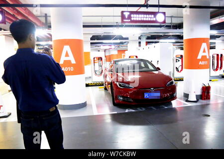 Un residente locale prende le foto di una Tesla auto elettrica essendo addebitato al mondo la più grande stazione di sovralimentazione di Tesla all'interno di un parcheggio sotterraneo Foto Stock