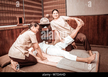 Due massaggiatrici stretching gambe per il loro cliente. Foto Stock