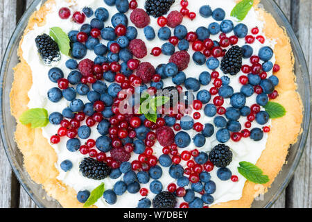 Crostata con mirtilli freschi, lamponi, more, ribes rosso panna montata e decorate con foglie di menta. Vista da sopra Foto Stock