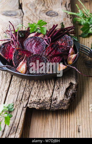 Homegrown barbabietole tostate e aglio in padella in ghisa, prezzemolo fresco erbe su legno tavolo rustico, impianti alimentari a base dei prodotti locali, vicino. Pergamo Foto Stock