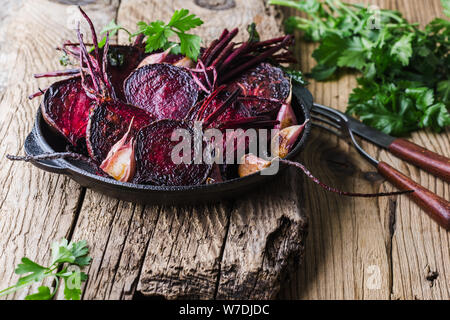 Homegrown barbabietole tostate e aglio in padella in ghisa, prezzemolo fresco erbe su legno tavolo rustico, impianti alimentari a base dei prodotti locali, vicino. Pergamo Foto Stock