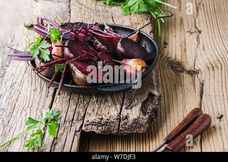 Homegrown barbabietole tostate e aglio in padella in ghisa, prezzemolo fresco erbe su legno tavolo rustico, impianti alimentari a base dei prodotti locali, vicino. Pergamo Foto Stock