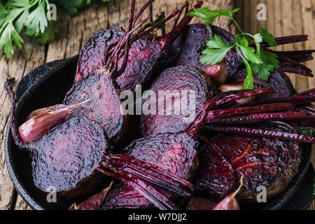 Homegrown barbabietole tostate e aglio in padella in ghisa, prezzemolo fresco erbe su legno tavolo rustico, impianti alimentari a base dei prodotti locali, vicino. Pergamo Foto Stock