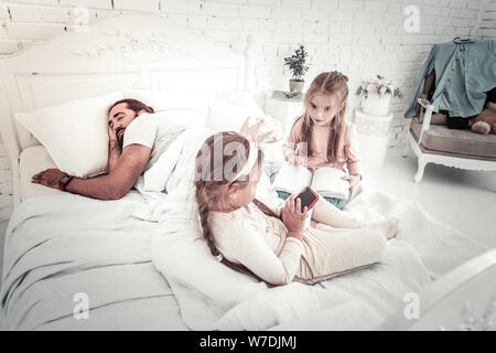 Due sorelle divertirsi sul letto mentre il loro padre dorme Foto Stock