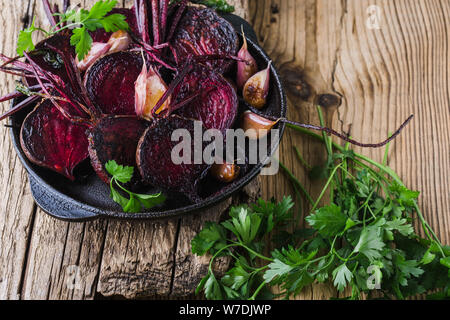 Homegrown barbabietole tostate e aglio in padella in ghisa, prezzemolo fresco erbe su legno tavolo rustico, impianti alimentari a base dei prodotti locali, vicino. Pergamo Foto Stock