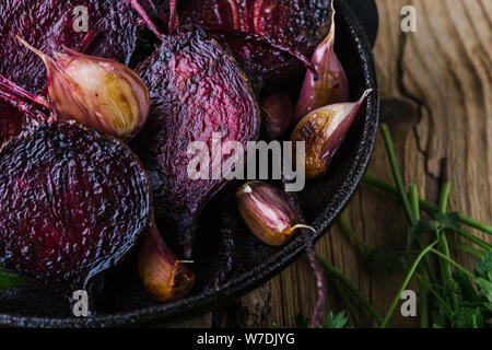 Homegrown barbabietole tostate e aglio in padella in ghisa, prezzemolo fresco erbe su legno tavolo rustico, impianti alimentari a base dei prodotti locali, vicino. Pergamo Foto Stock