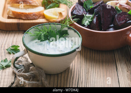 Yogurt dip con prezzemolo e aneto e succo di limone servita su tavola in legno rustico con arrosti di barbabietole, pane e limone fresco acqua, vicino, vegan impianto bas Foto Stock